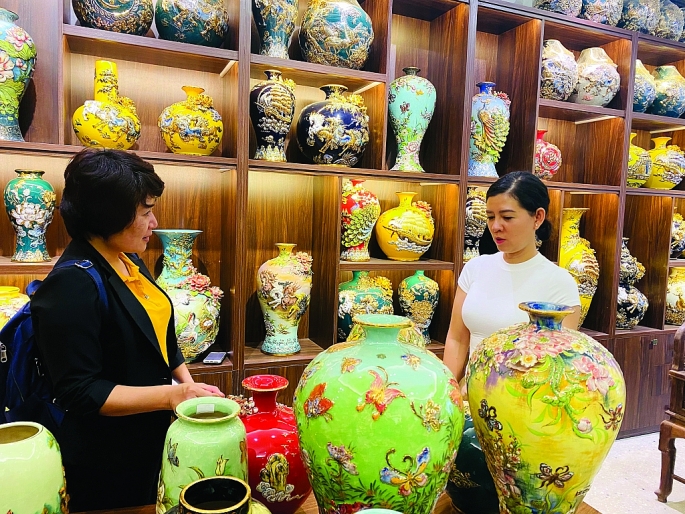 Nghệ nhân Vũ Như Quỳnh đang giới thiệu sản phẩm gốm đắp nổi cho du khách, tại làng gốm Bát Tràng.               Ảnh Nguyễn Vũ