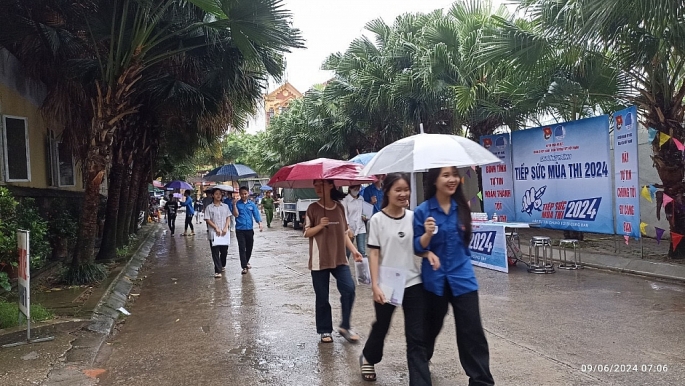 Hỗ trợ thí sinh đến điểm thi dưới trời mưa nặng hạt, sáng 9/6. Ảnh: Văn Biên